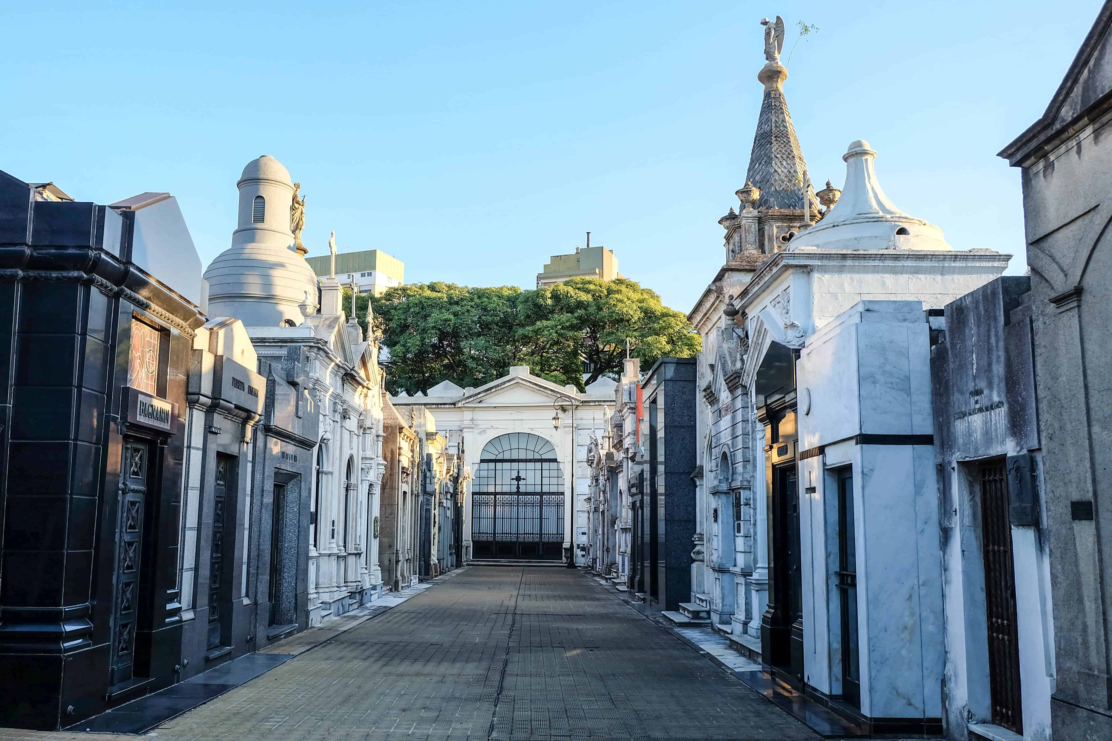布宜諾斯艾利斯雷科萊塔墓園 壁紙 — 一條陽光普照的大道，兩旁是裝飾華麗的白色和黑色墳墓，通向歷史墓園的大門入口。
