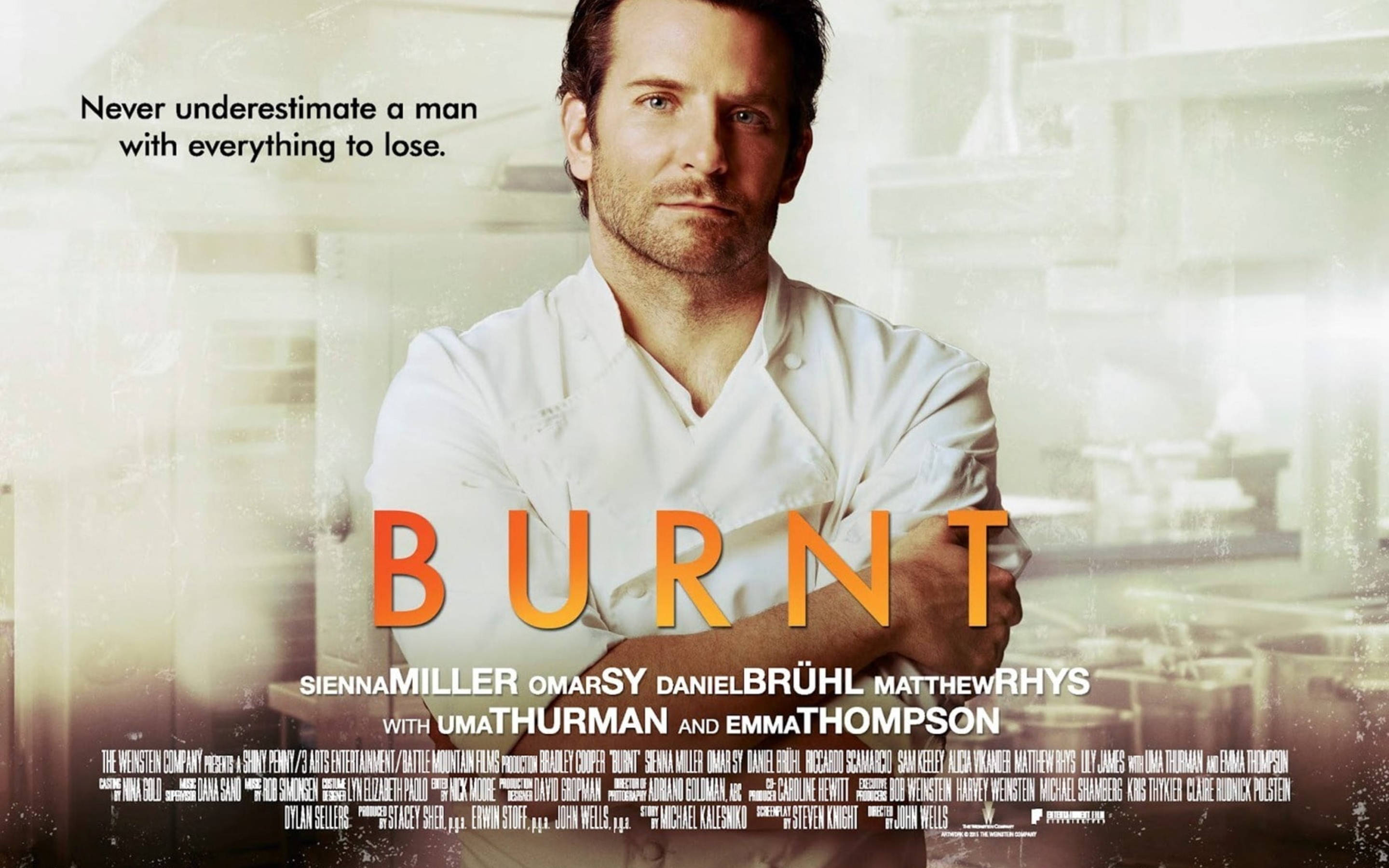布拉德利·庫珀《Burnt》廚師服造型 壁紙 — 一位嚴肅的廚師穿著白色外套，雙臂交叉站在模糊的廚房裡，標題「BURNT」在溫暖朦朧的背景上發出橙色光芒。