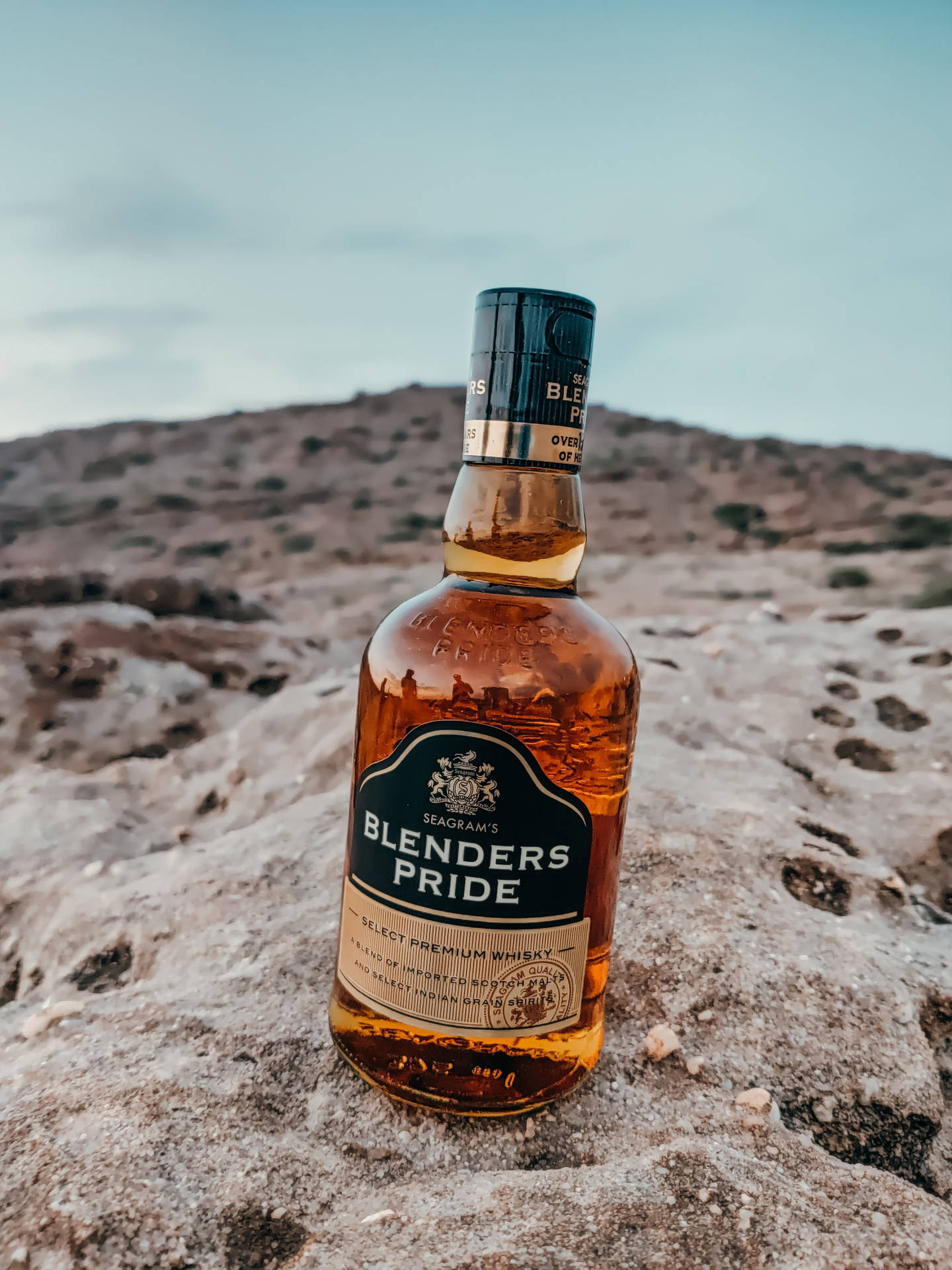 Blenders Pride 威士忌酒瓶在沙漠岩石上，暮色中