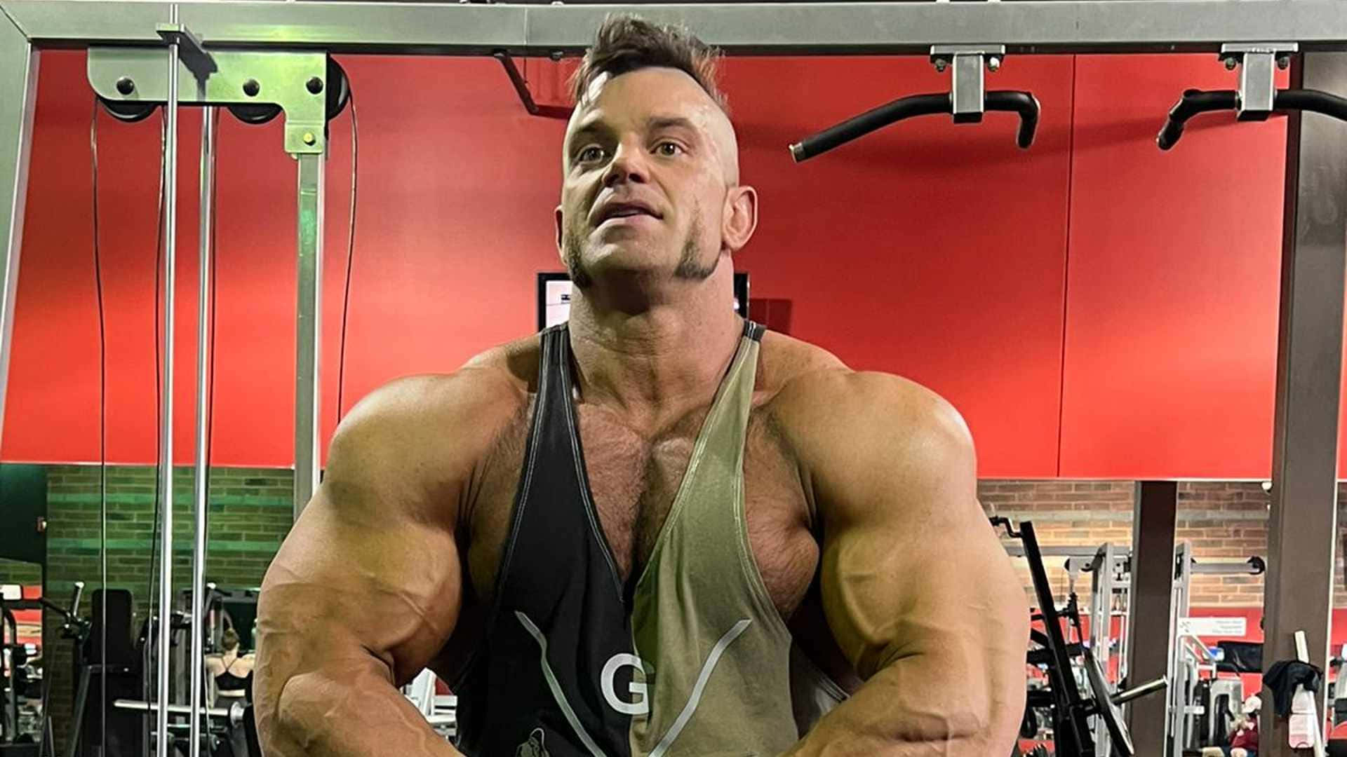 一個肌肉發達的男人在紅色牆壁的健身房中展示二頭肌。