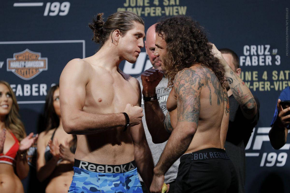 兩名MMA拳手在UFC過磅活動中，背景有粉絲和標誌，互相凝視。