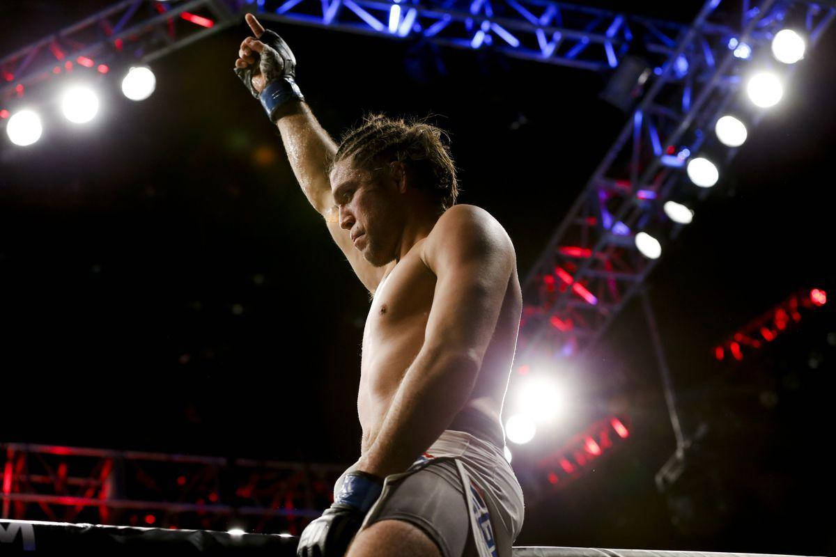 拳擊手在明亮的MMA八角籠中舉起拳頭慶祝勝利。