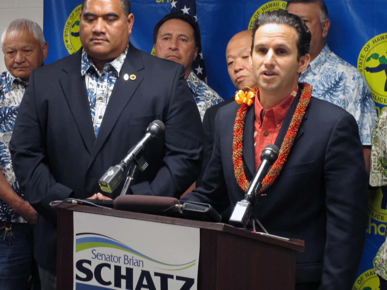 布萊恩·沙茲競選期間 壁紙 — 參議員 Brian Schatz 在記者會上發言，戴著花環，站在顯示他名字的講台上。
