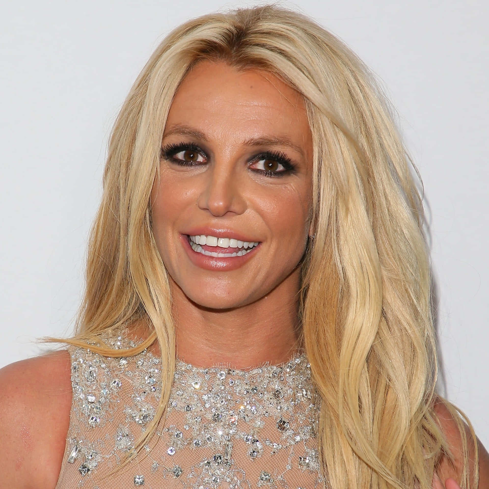 Britney Spears 穿著閃亮上衣，長長的金色頭髮，微笑著。