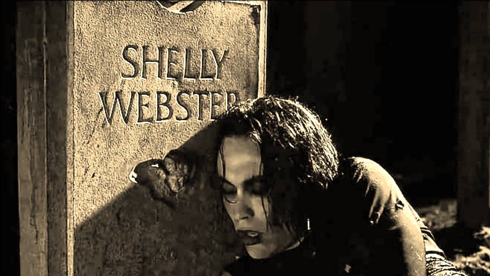 女人在昏暗的墓園中，將頭靠在名為Shelly Webster的墓碑上休息。