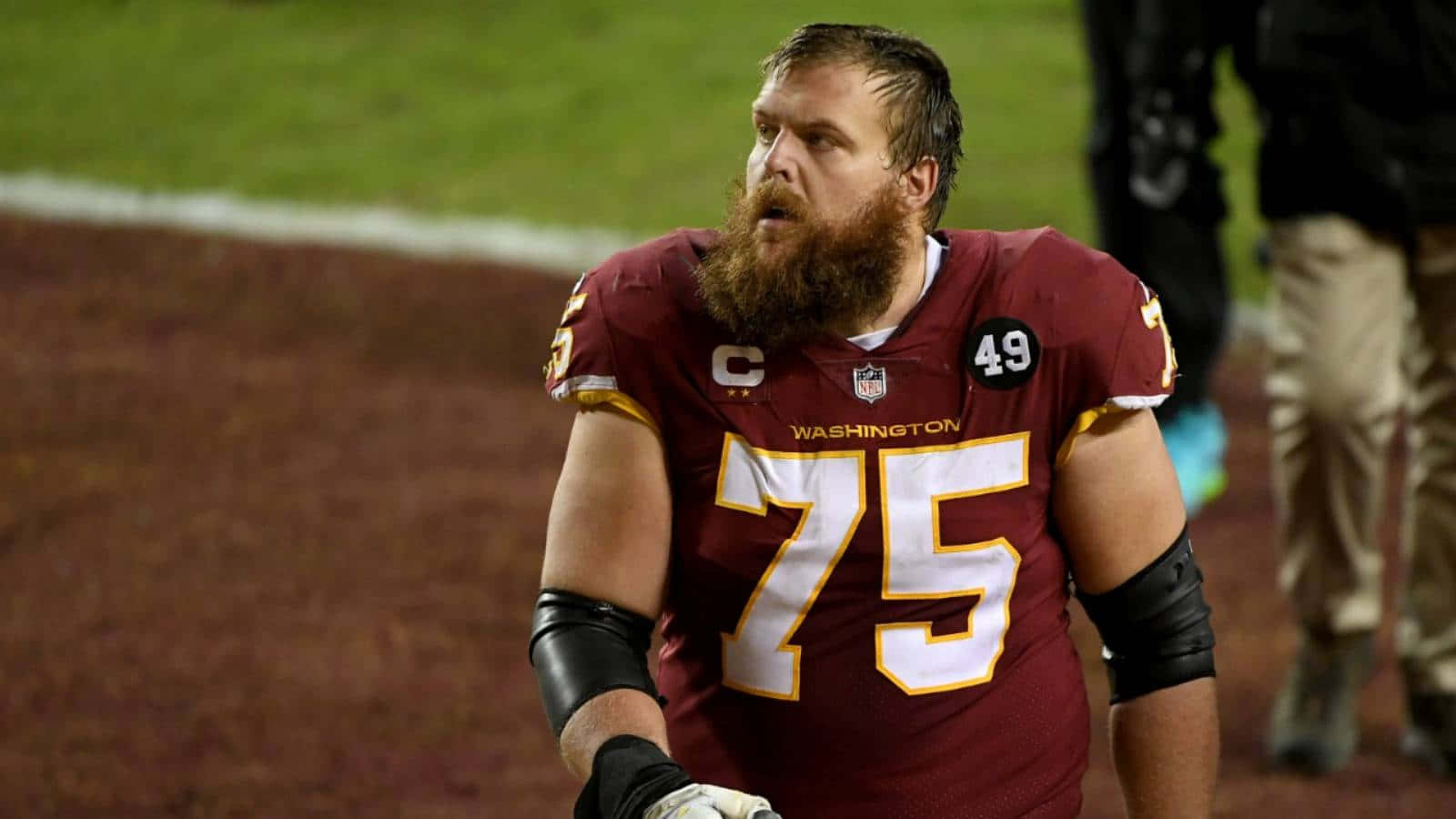 布蘭登·舍弗 對戰卡羅萊納黑豹隊 2020 壁紙 — 一位留鬍子的NFL進攻截鋒穿著酒紅色的華盛頓球衣，在夜間比賽中帶著專注的強度站在場上。