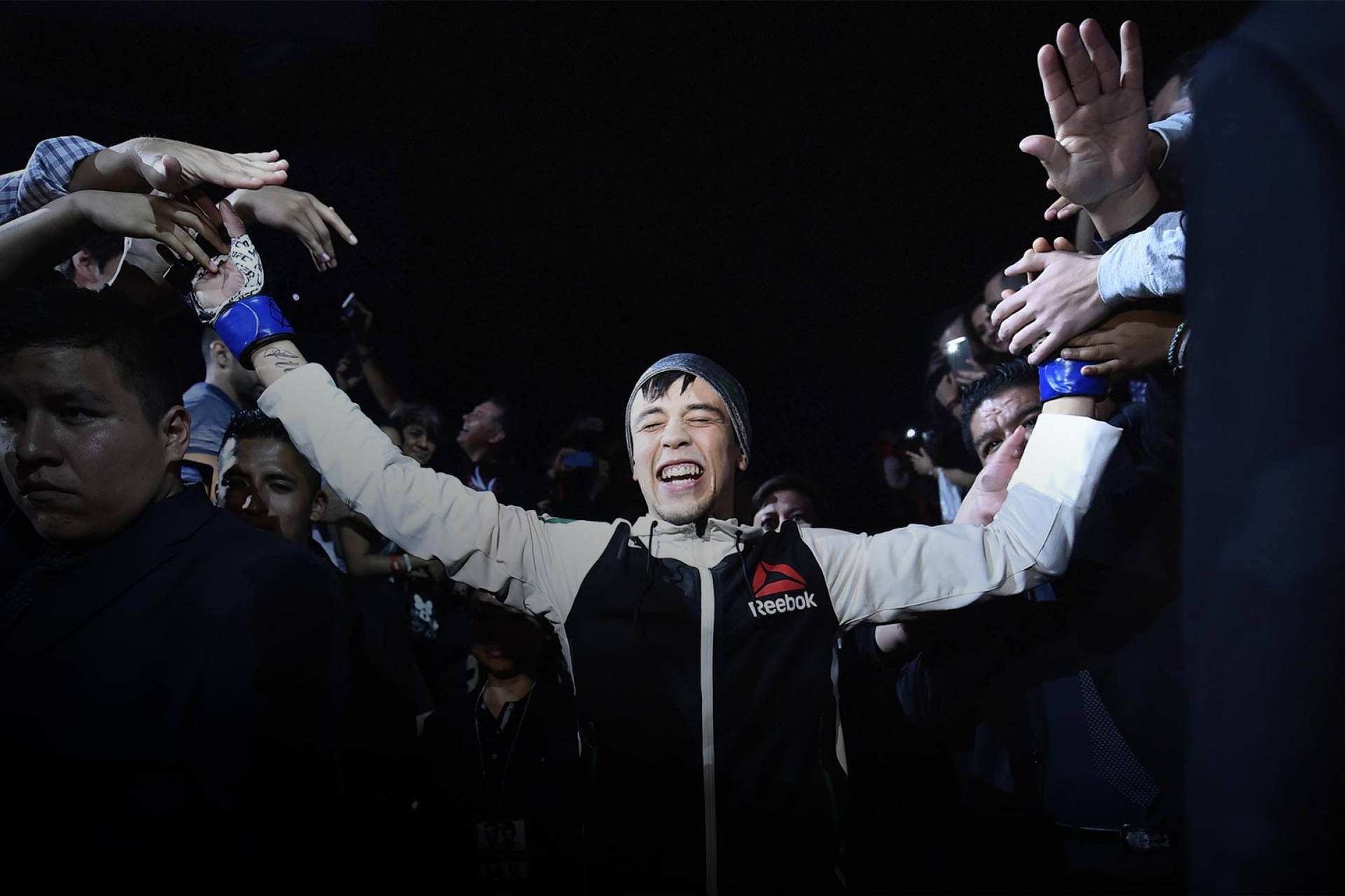 拳手舉起雙臂慶祝勝利，粉絲們伸手觸摸他的手套。
