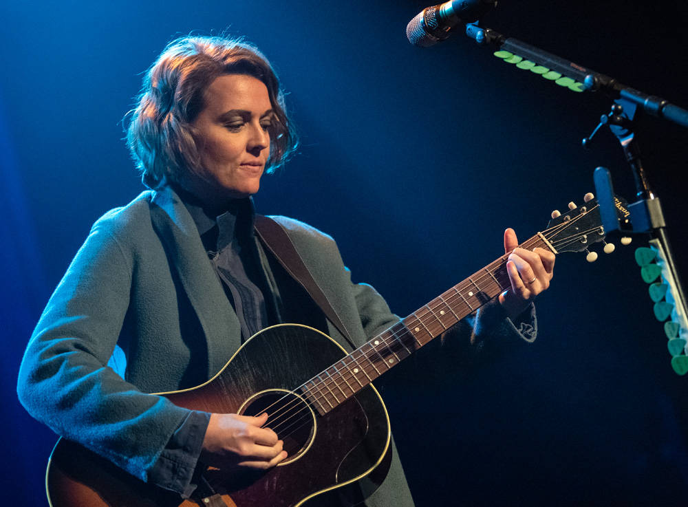 布蘭迪·卡莉現場演唱 壁紙 — 一位女音樂家在藍色舞台燈光下彈奏木結他，附近有一個麥克風。