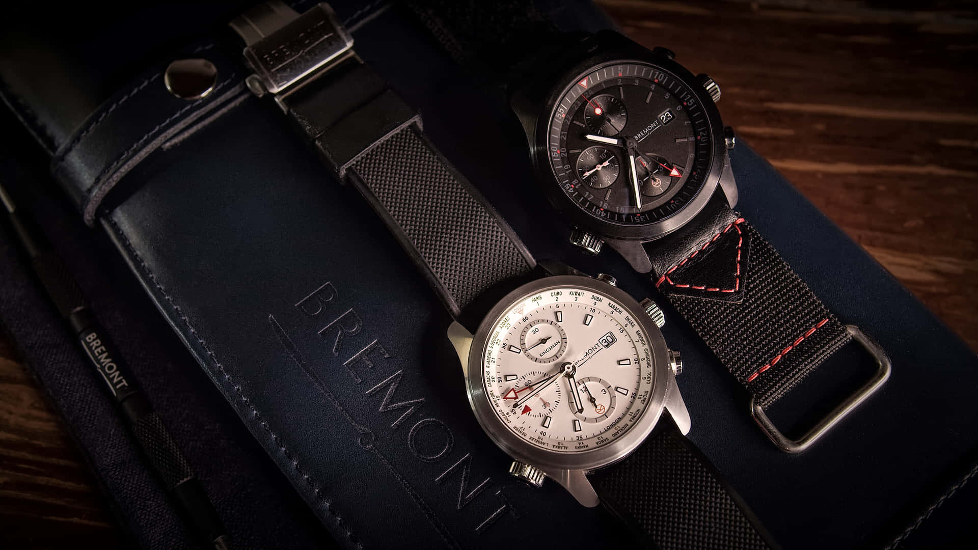 兩枚帶有紋理錶帶的Bremont手錶放在木質上的海軍藍皮革錶盒上。