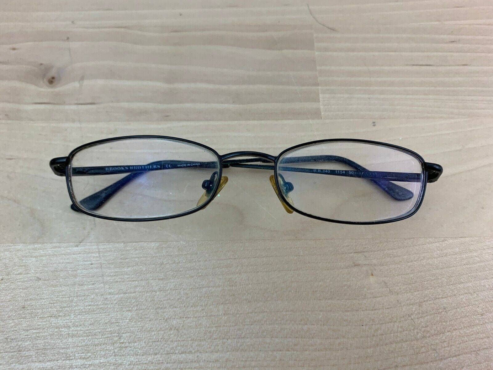 布魯克斯兄弟藍色鏡框眼鏡 壁紙 — 一副黑色鏡框的Brooks Brothers閱讀眼鏡放在淺色木紋表面上。