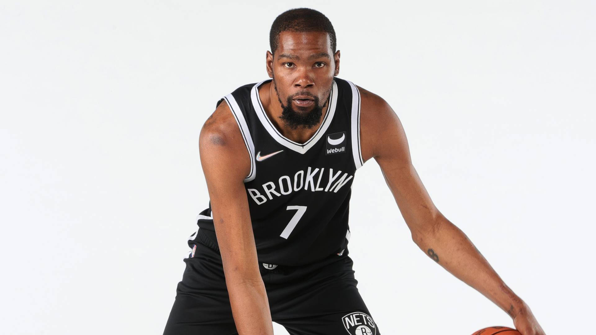 布魯克林籃網隊球員凱文·杜蘭特 壁紙 — 籃球運動員 Kevin Durant 身穿布魯克林籃網隊球衣，在純白色背景下蹲下，專注地拿著籃球。