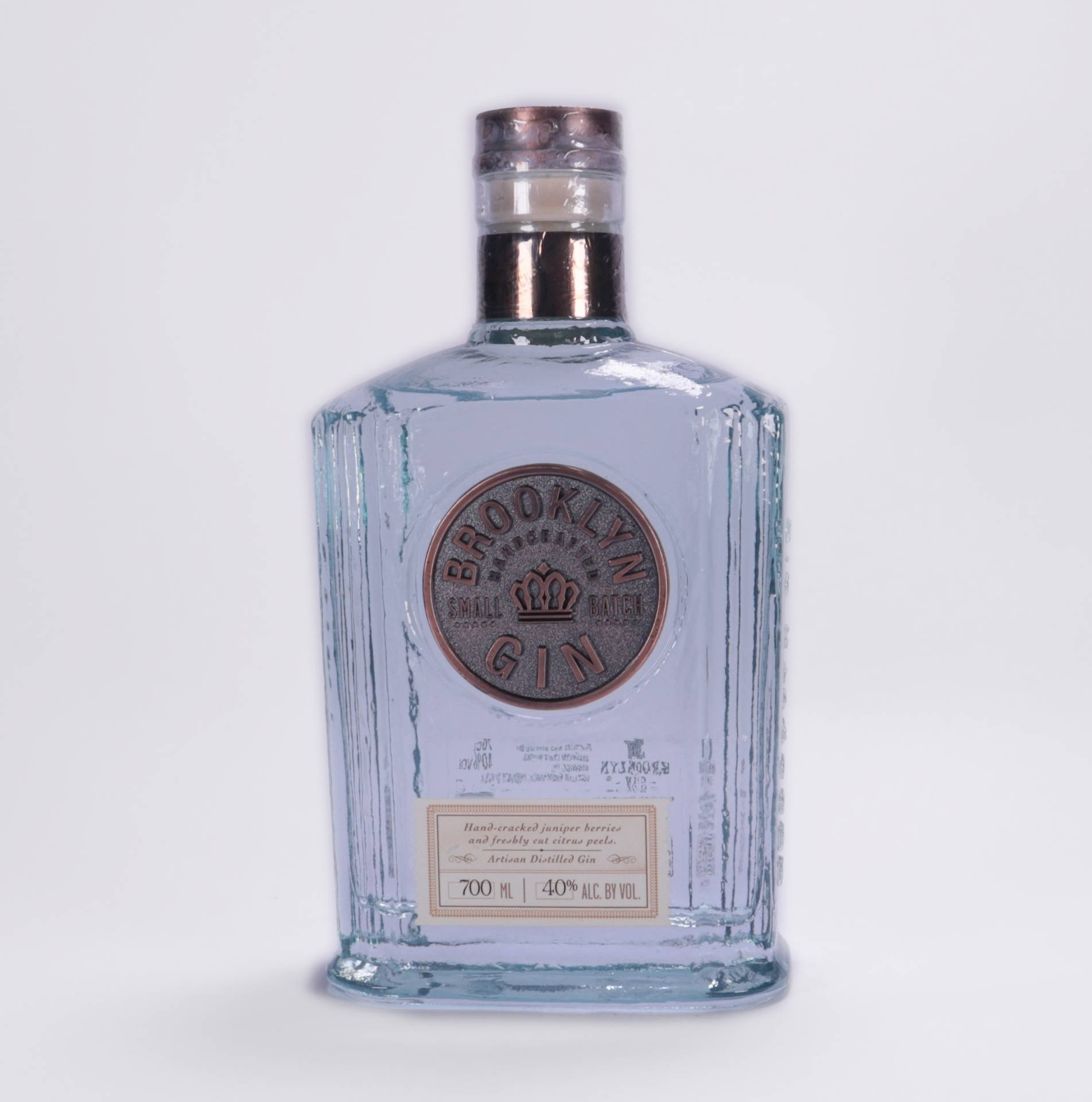 一個透明玻璃氈酒瓶，帶銅蓋和布魯克林標籤，白色背景。