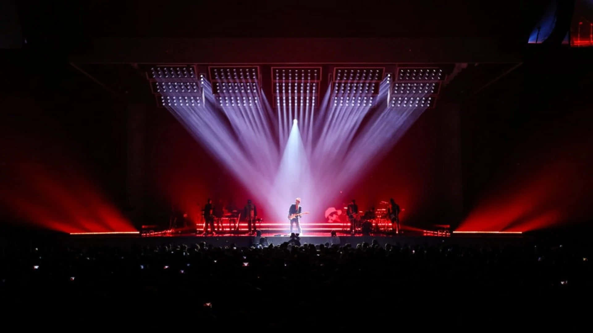 一位音樂家在燈火通明的舞台上表演，紅色聚光燈和黑暗中的觀眾。