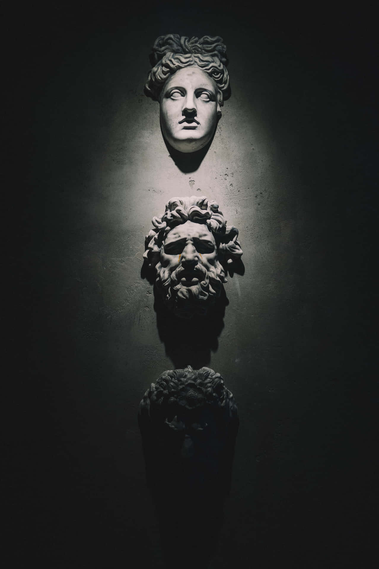 三個古代石像半身像在黑暗牆壁前被聚光燈照亮。