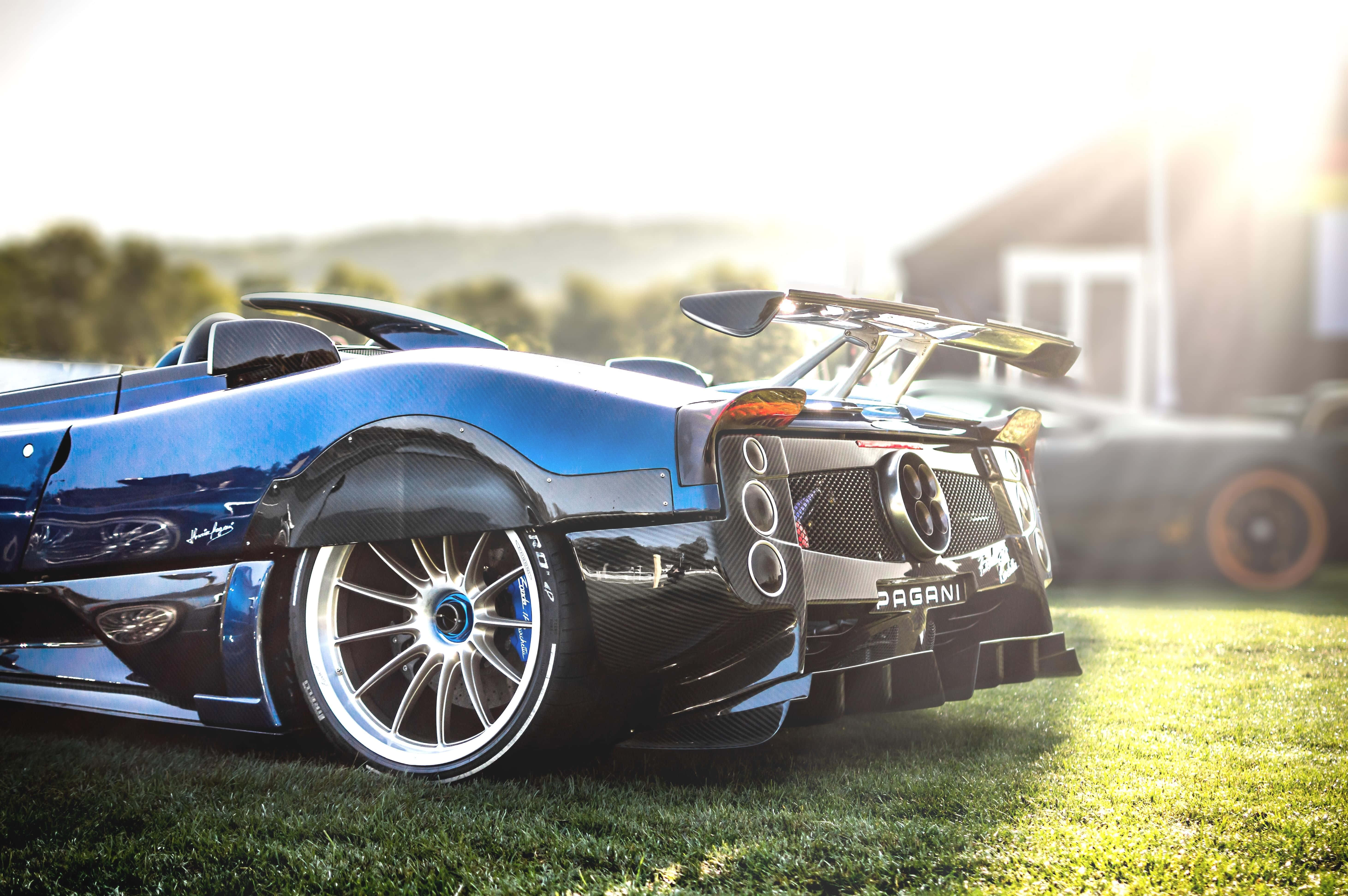帕加尼Zonda HP Barchetta全貌盡顯 壁紙 — 一輛時尚的藍色帕加尼 Huayra 跑車在金色日出光線下，以模糊的鄉村背景為襯托，在草地上閃閃發光。
