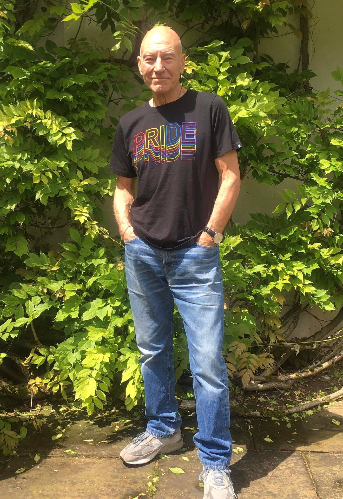 穿著驕傲T恤的男人站在綠色常春藤牆前