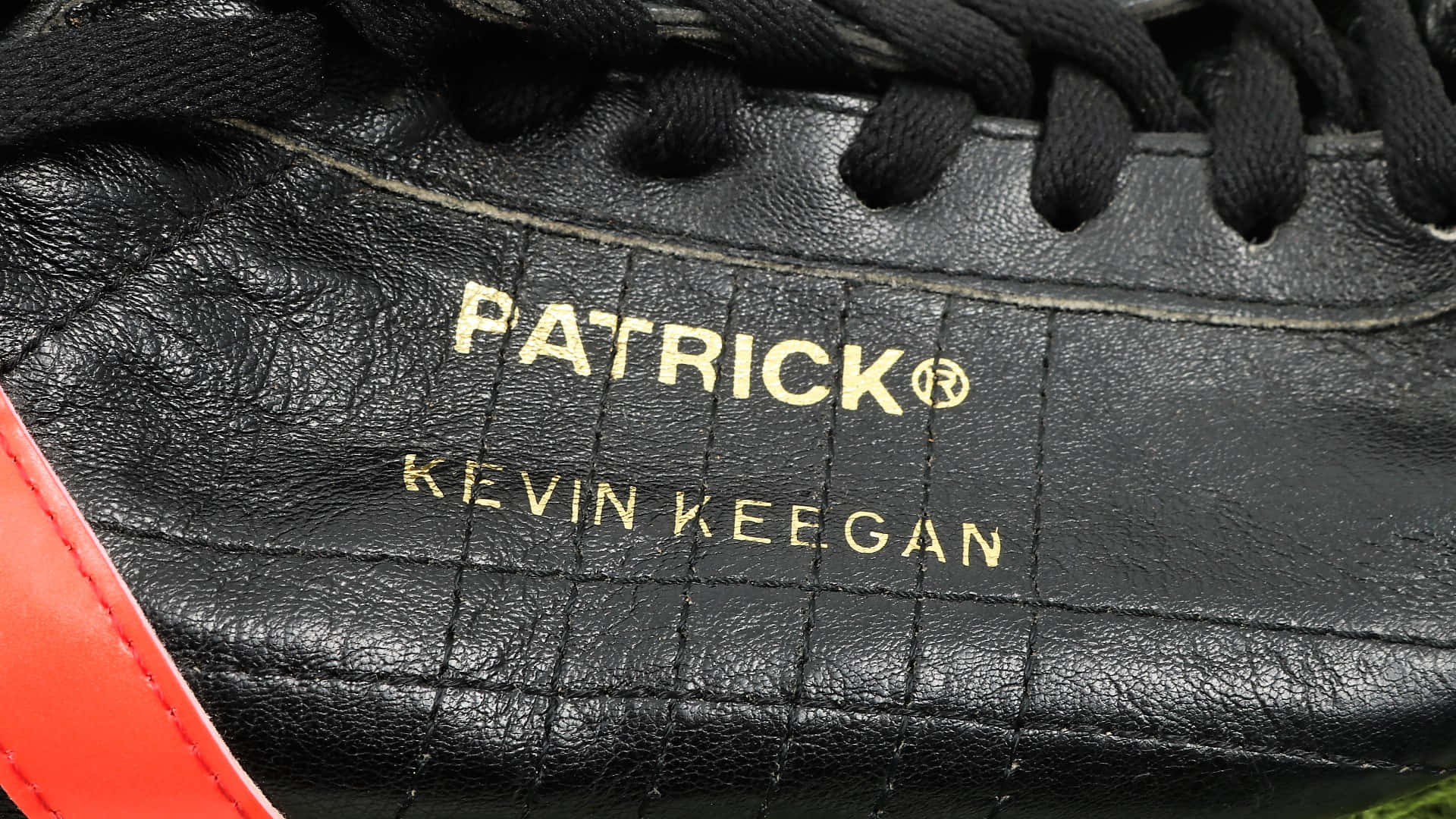 黑色皮革足球靴，帶有金色 Patrick Kevin Keegan 文字和紅色點綴。