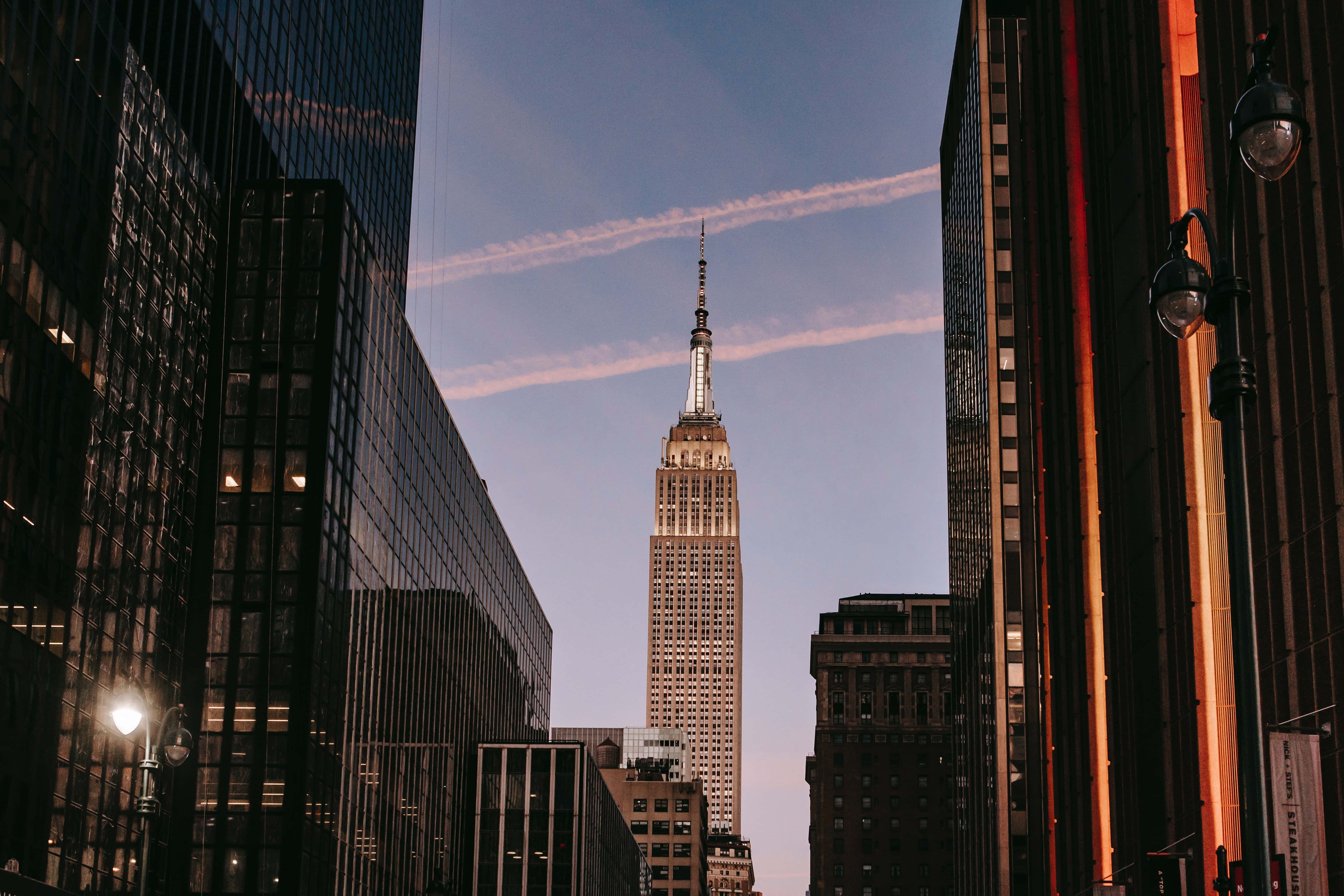 Nyc 桌布 壁紙 — 帝國大廈在暮色天空下，於高聳的摩天大樓之間雄偉地崛起，天空帶有柔和粉紅與藍色條紋。