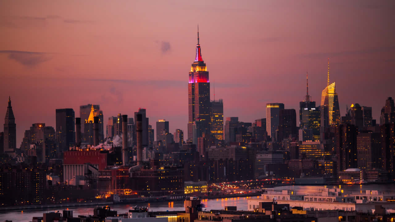 帝國大廈夜景，紐約地標建築 壁紙 — 紐約市天際線在黃昏時分，帝國大廈在柔和的紫色天空映襯下閃耀著粉紅色和金色。