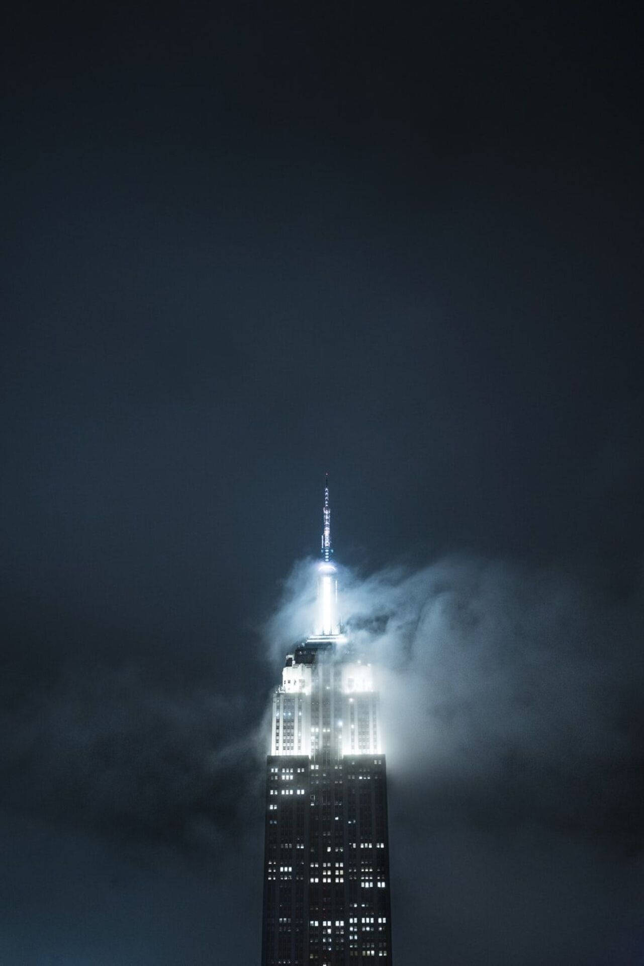 高聳的帝國大廈在夜間透過烏雲亮起。 — 主螢幕 壁紙