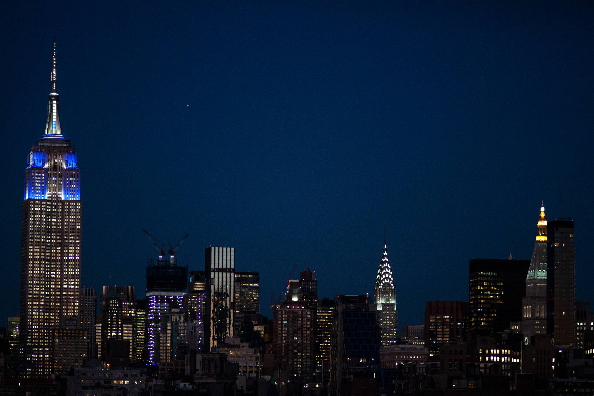 紐約市夜景天際線，摩天大樓燈火通明，黑暗天空中可見一顆星星。