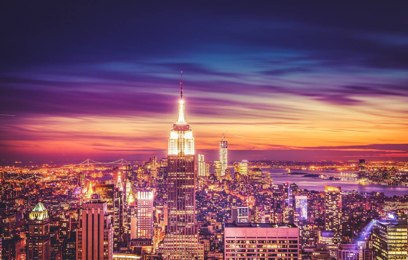 帝國大廈閃耀夜景 壁紙 — 紐約市天際線的 vibrant 日落，帝國大廈在紫色和橙色條紋雲層中閃耀。