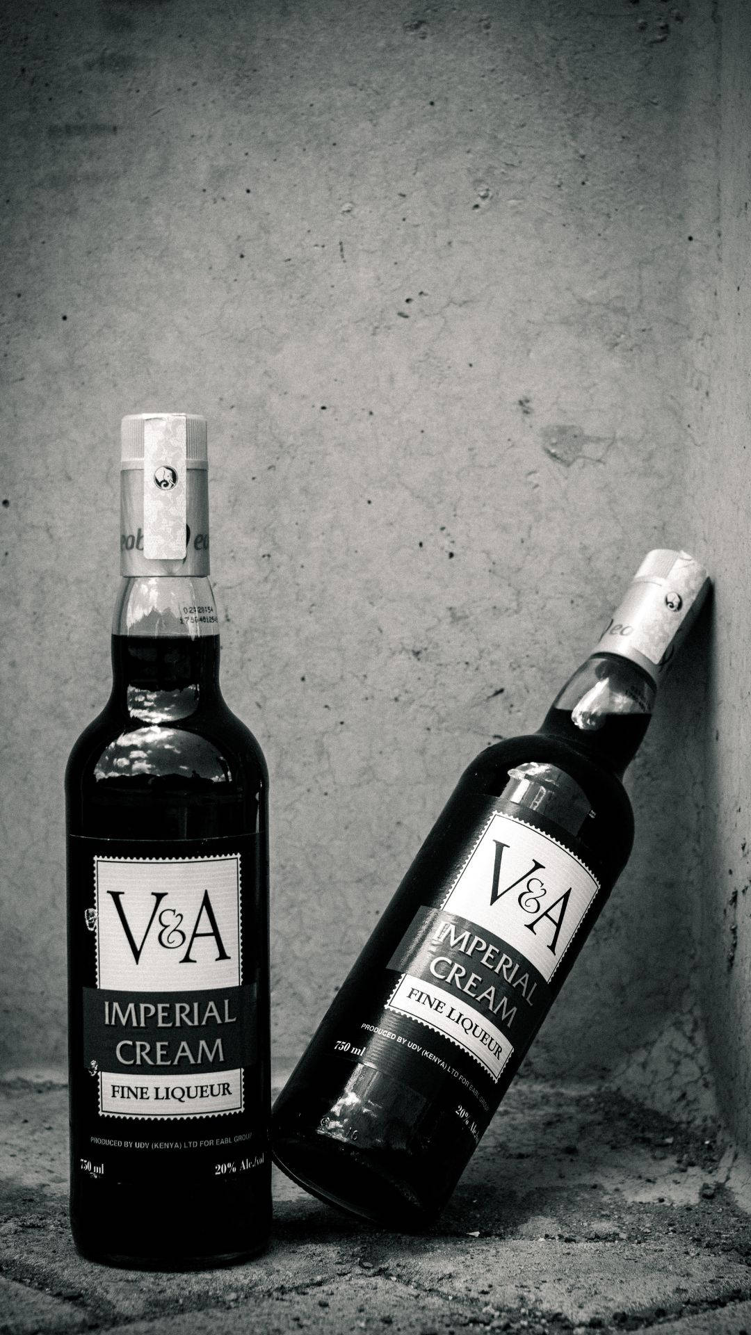 帝國奶油酒黑白攝影 壁紙 — 兩瓶V&A Imperial Cream利口酒，一瓶直立，一瓶靠著紋理混凝土牆，單色調。