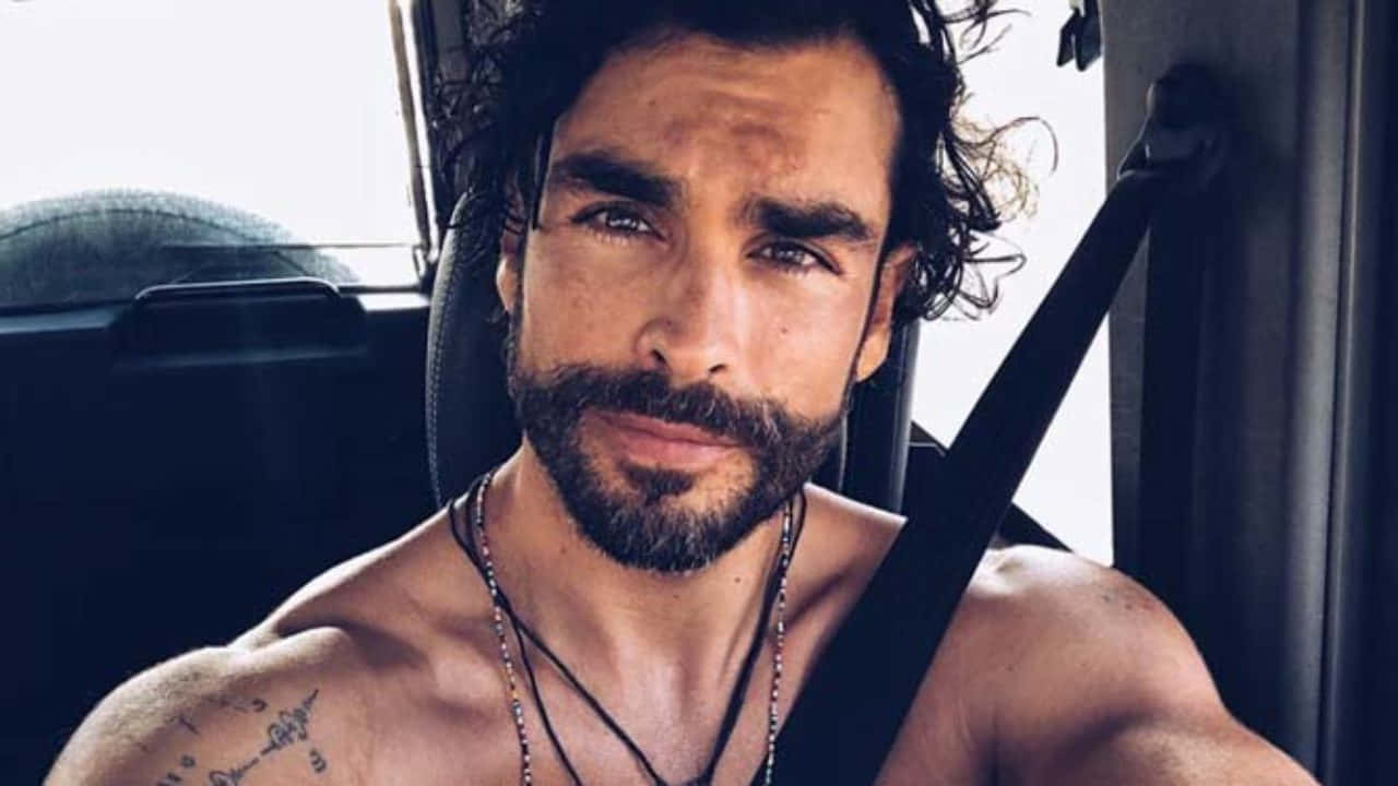 帥氣男士 Gonzalo García Vivanco 自拍 壁紙 — 一個冇著衫、有鬍鬚同紋身嘅男人，喺陽光穿過車窗嘅車入面自信咁望住鏡頭。