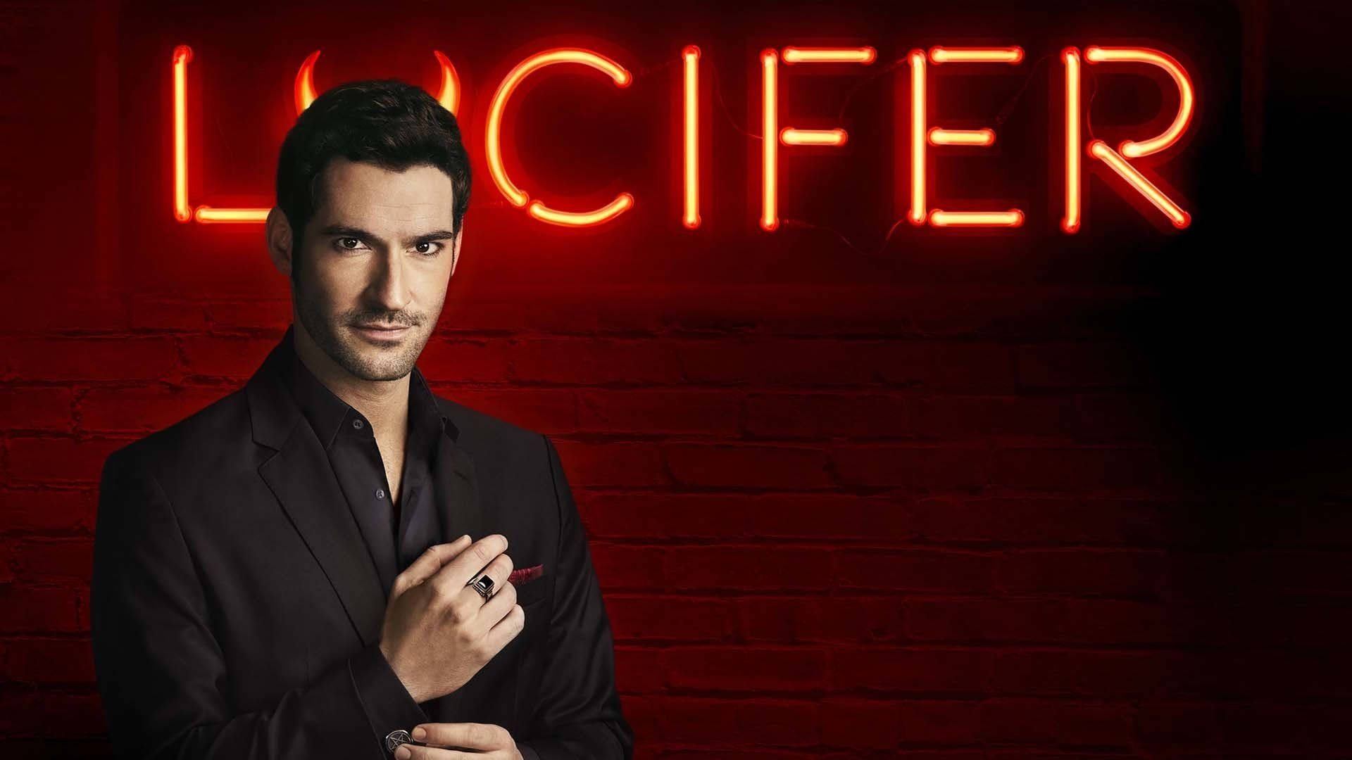 身穿黑色西裝的男子在磚牆上的紅色霓虹燈 Lucifer 標誌下拿著筆。