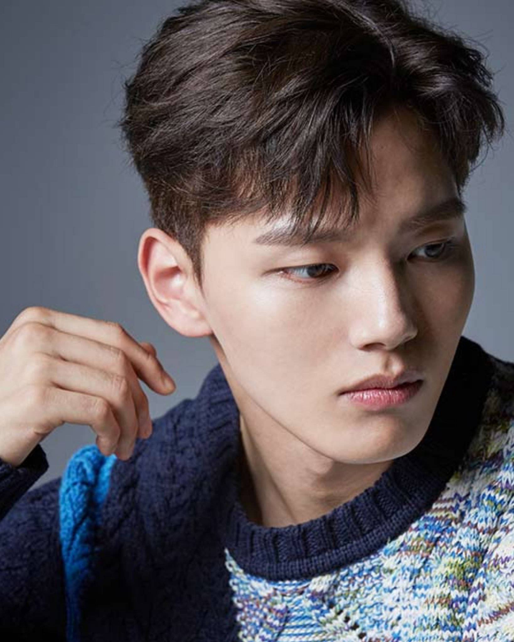 帥氣短髮 Yeo Jin Goo 壁紙 — 一位深色頭髮的年輕男子，穿著彩色針織毛衣搭在深藍色毛衣上，若有所思地凝視著。