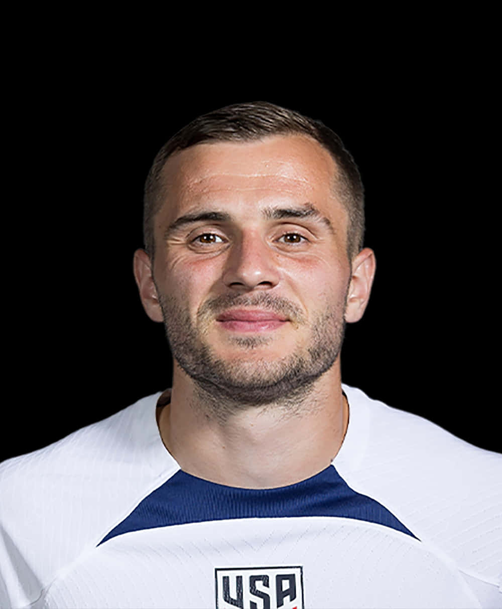 帥氣美國足球員 Jordan Morris 獨照 壁紙 — 一位身穿白色美國球衣的男性足球員在黑色背景前的特寫肖像。