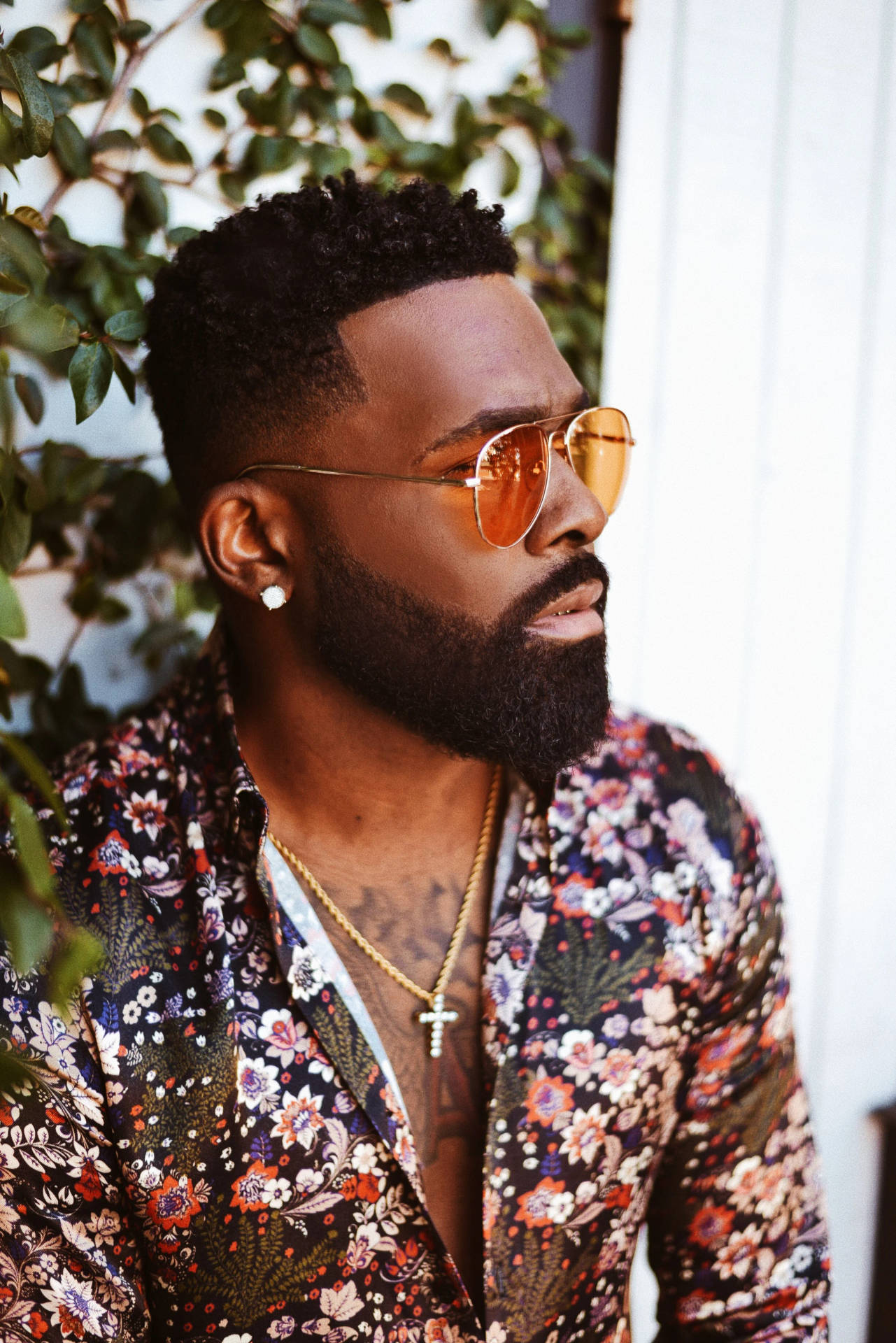 男士穿著花襯衫和飛行員太陽眼鏡，留鬍子，佩戴金色首飾。
