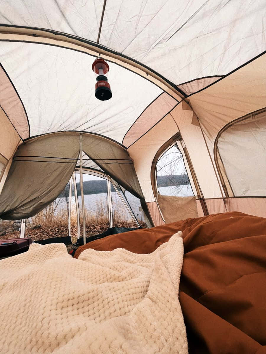 Minimalist Camping 桌布 壁紙 — 帳篷內部舒適，掛著燈籠，下方是棕色睡袋和質感毛毯，俯瞰平靜的湖泊。
