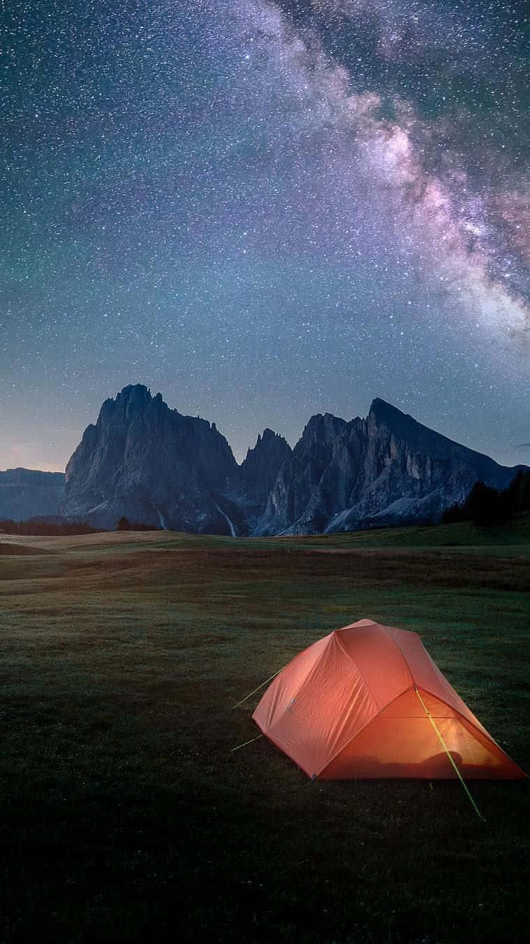 一個發光的橙色帳篷在星空下，銀河在山脈上空