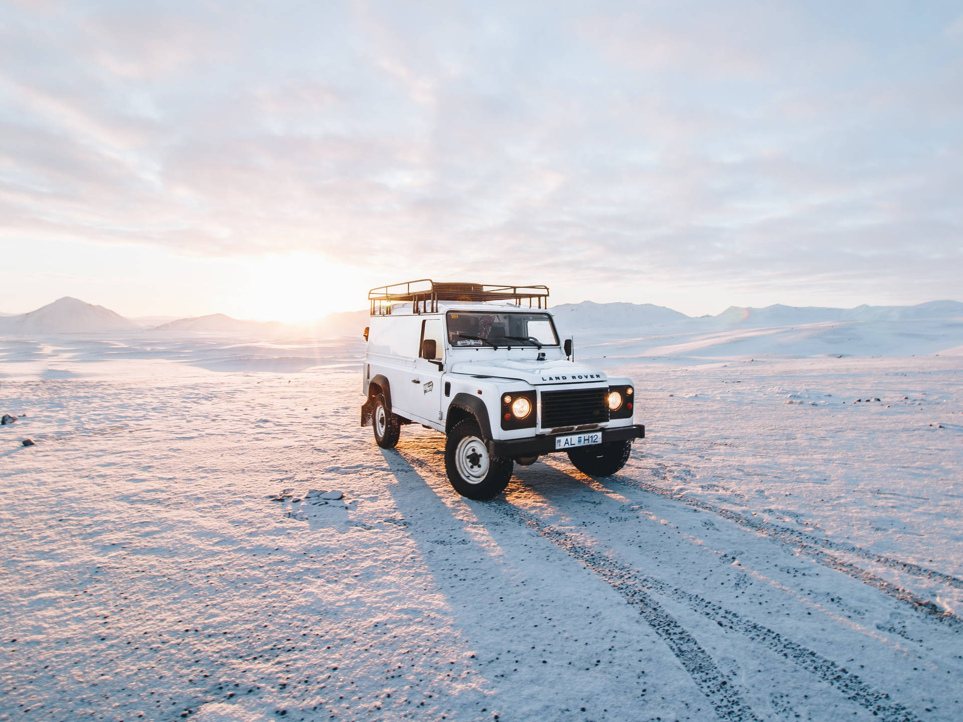 白色 Land Rover Defender 在日出時分駛過雪覆蓋的沙漠，背景有山。