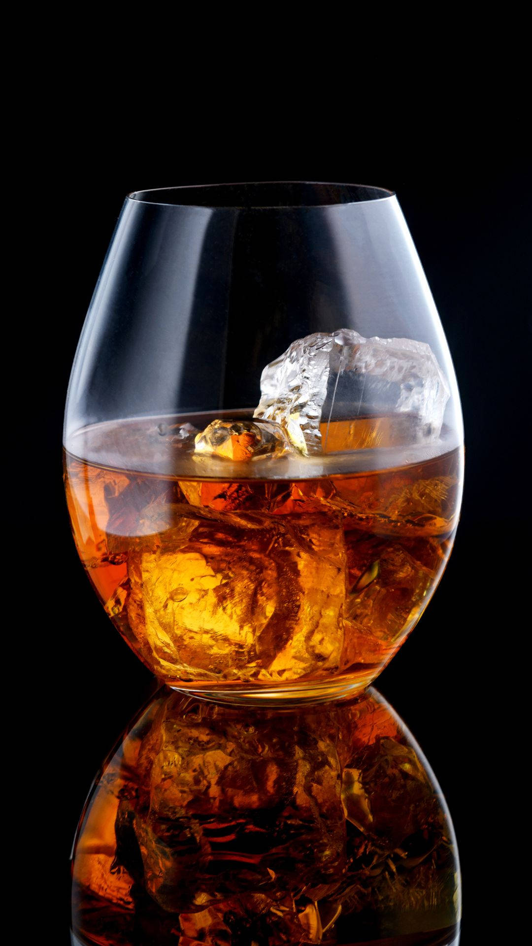 帶冰塊的琥珀色酒精杯 壁紙 — 一杯琥珀色威士忌配上大冰塊，在黑色背景上閃耀，下方有完美倒影。