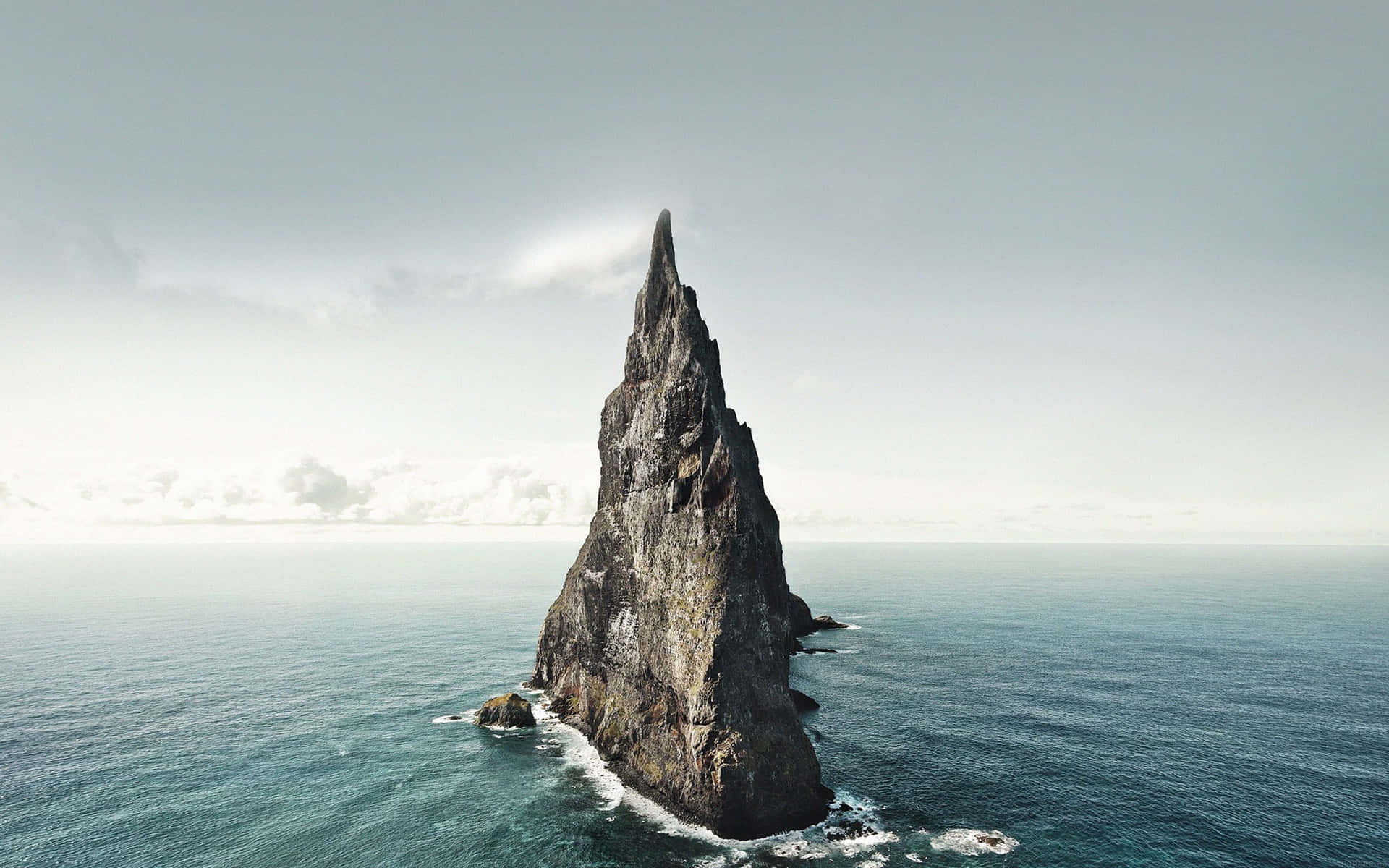 一座高高的岩石島嶼在陰天之下孤獨地矗立在海中。