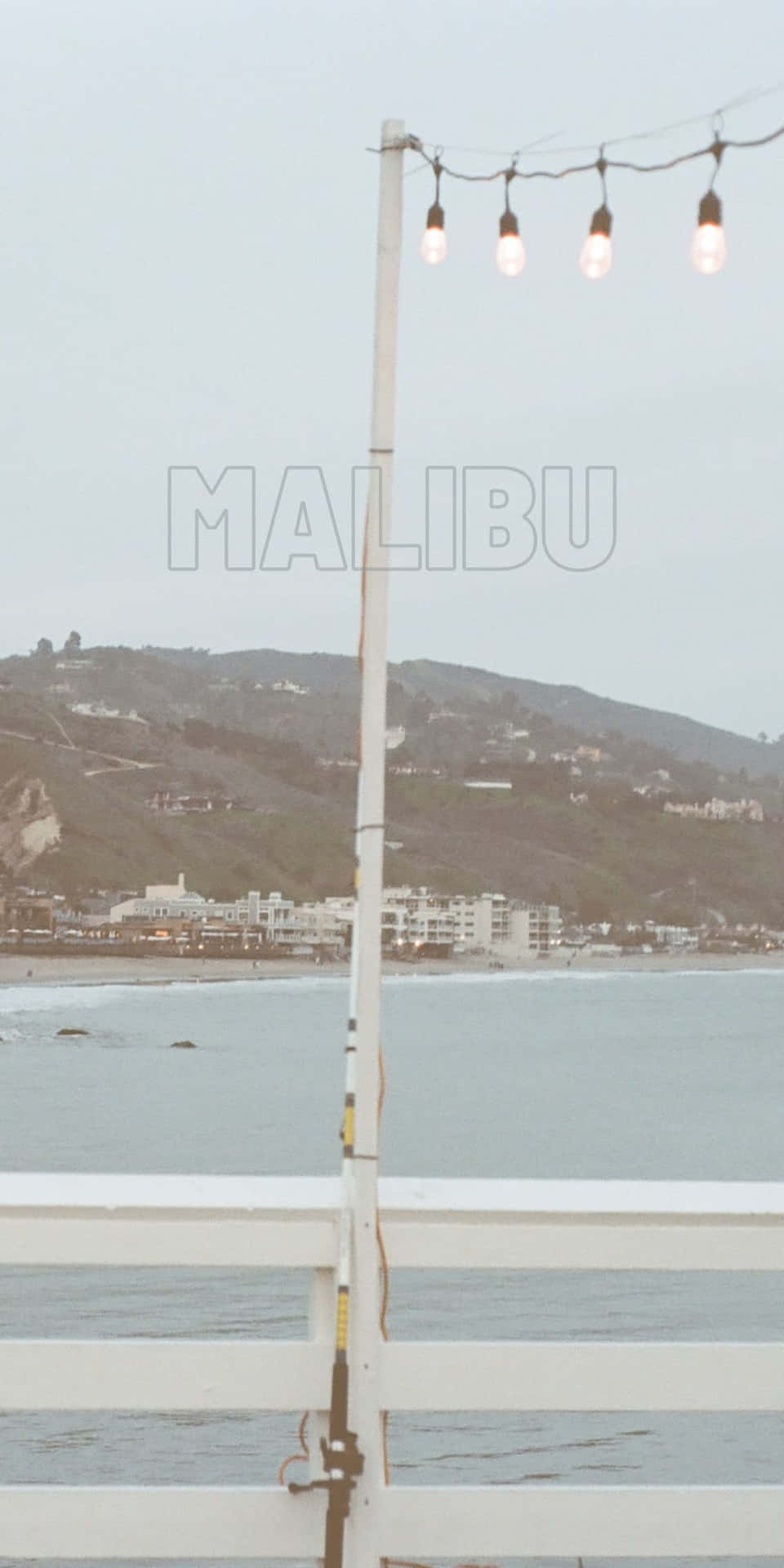 白色圍欄上的一串串燈光俯瞰霧氣瀰漫的馬里布海灘和山丘。
