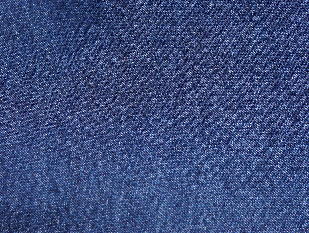 Denim Blue 桌布 壁紙 — 帶有可見編織紋理和細微褪色的質感靛藍牛仔布料的特寫。