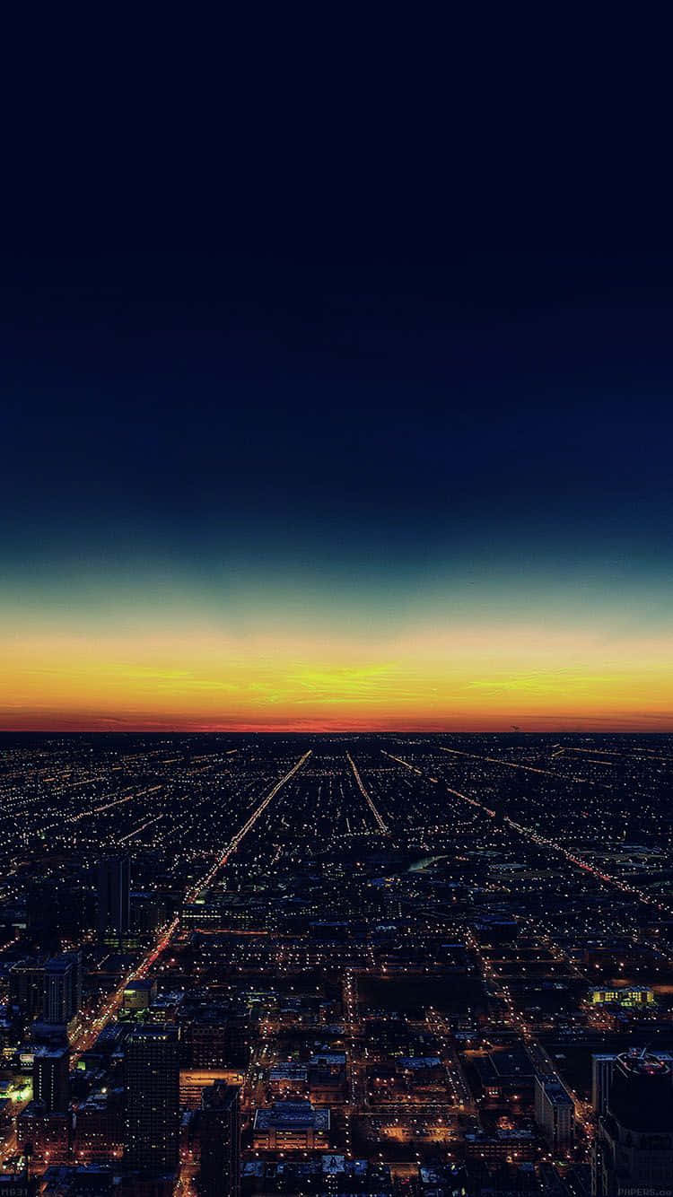 帶有摩天大樓與城市燈光的夕陽 iPhone 美學 壁紙 — 黃昏時分廣闊城市的鳥瞰圖，閃爍的路燈和從深藍色漸變到火橙色的天空。