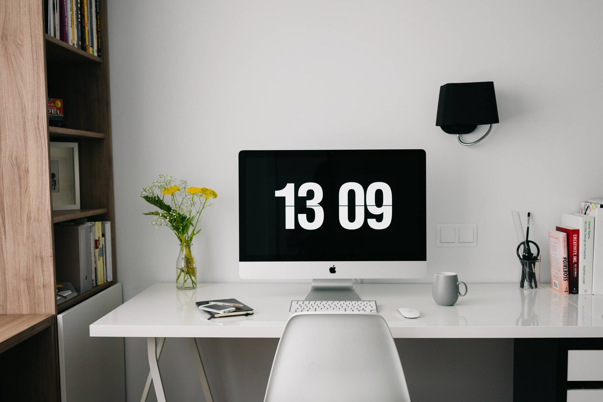 乾淨現代的書桌，iMac 顯示日期 13 09，周圍環繞書籍和鮮花。