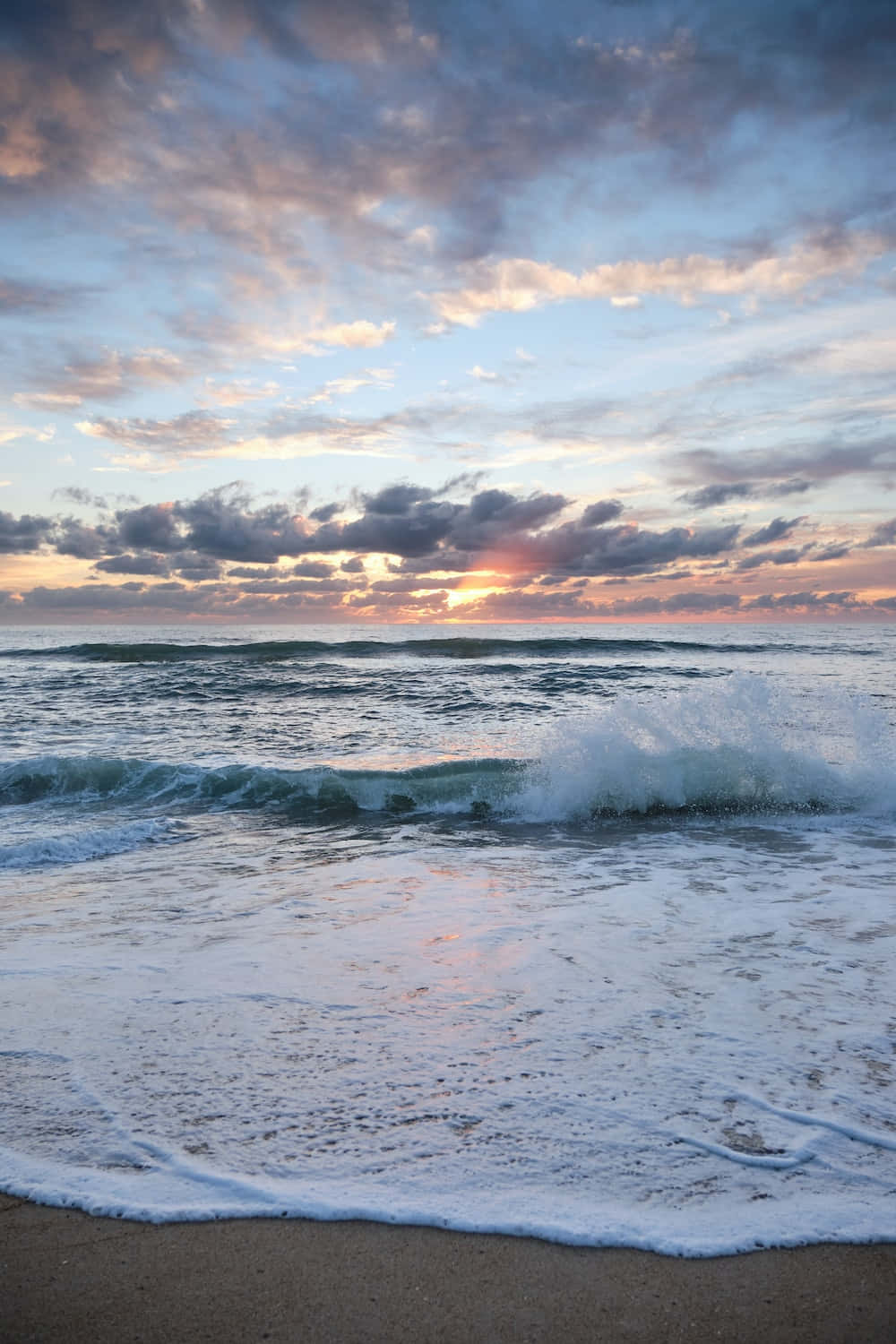 帶有氣泡波浪的夕陽海景美學圖 壁紙 — 夕陽將天空染成柔和的粉紅色和紫色，海浪拍打著沙灘。