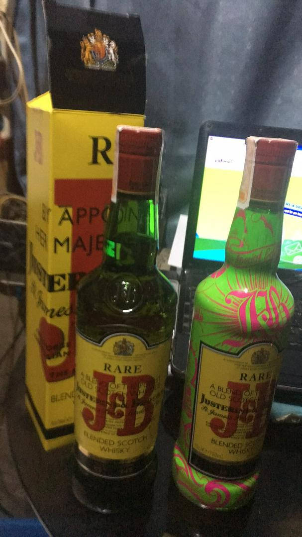 兩瓶 J&B 威士忌，一瓶標準款，一瓶彩色款，放在桌子上，旁邊是一部手提電腦和一個盒子。