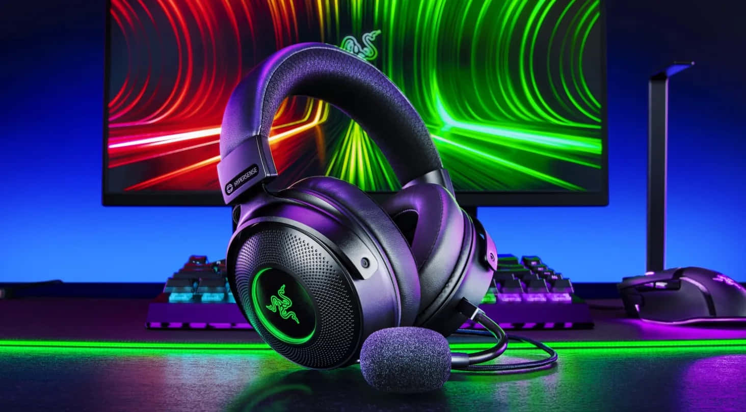 Gaming Headsets 桌布 壁紙 — 帶有綠色發光標誌的遊戲耳機放在桌上，前方是充滿活力的RGB照明顯示器和鍵盤。