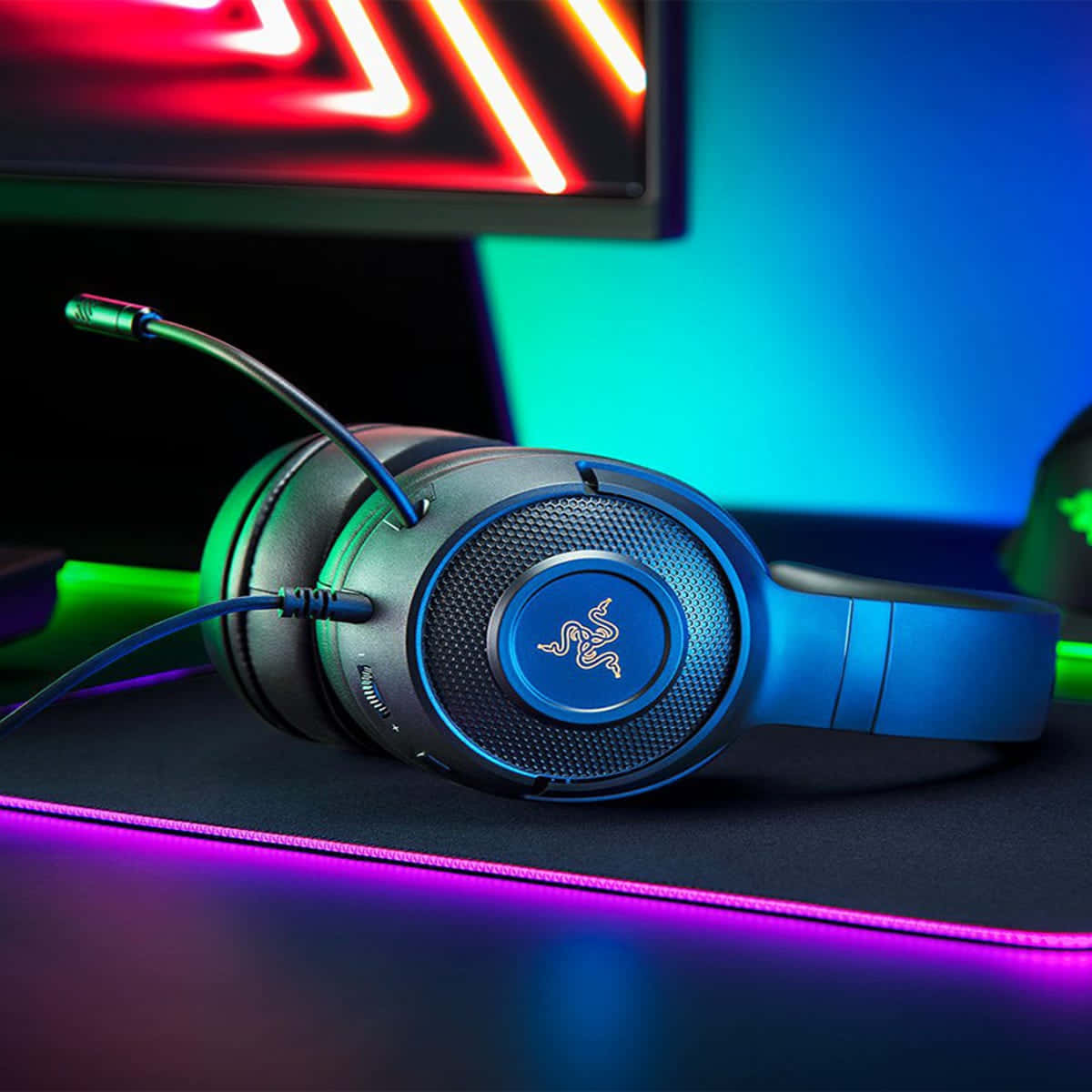 Gaming Headsets 桌布 壁紙 — 帶有藍色發光裝飾的遊戲耳機，放置在由鮮豔霓虹燈和RGB燈光照亮的桌子上。