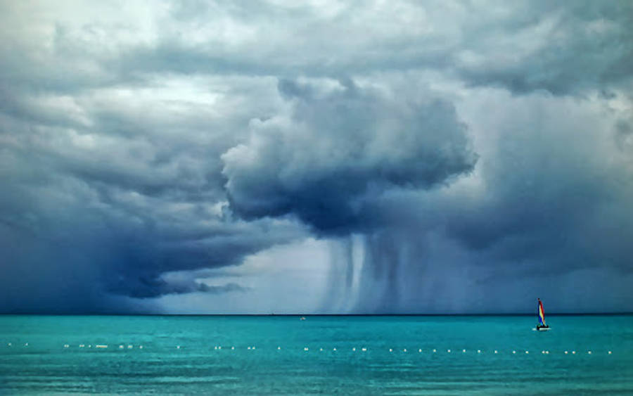 帶有雨勢的颶風 壁紙 — 一艘孤獨的帆船在傾盆大雨的巨大黑暗風暴雲下航行於碧綠色的水域。