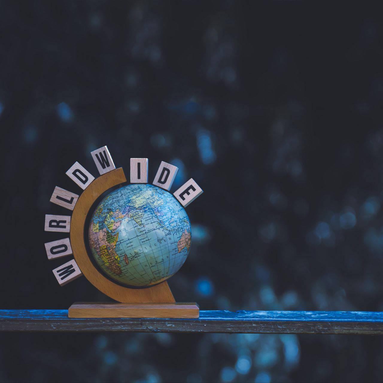 小地球儀與 'WORLDWIDE' 字母，放在深色架子上，藍色散景背景。