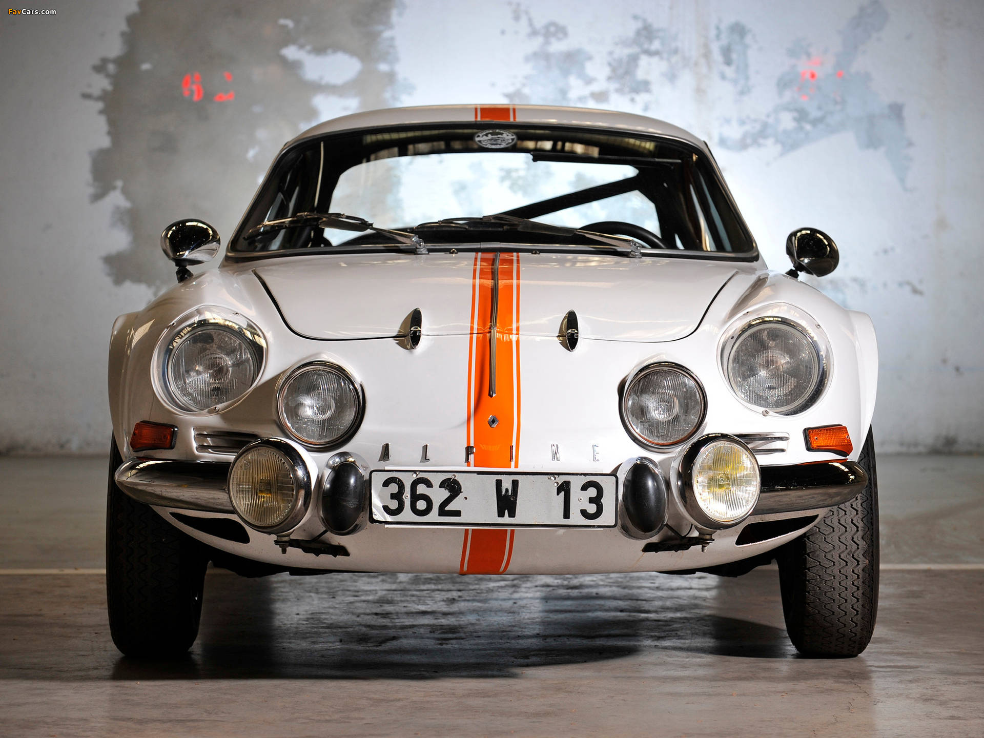 在混凝土車庫中，帶有橙色條紋的復古白色Alpine A110賽車。