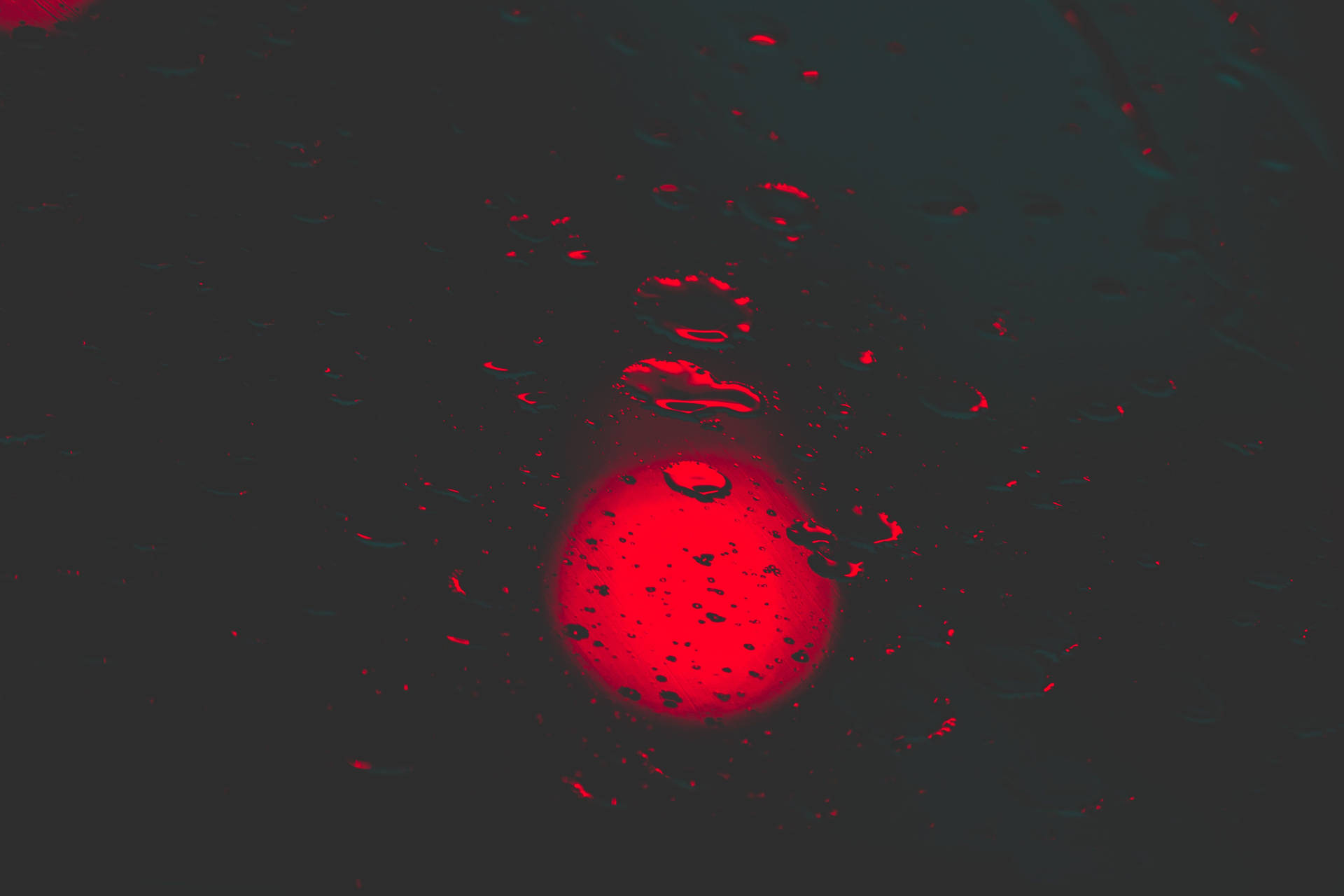 發光的紅色球體透過黑暗表面上的雨滴觀看。