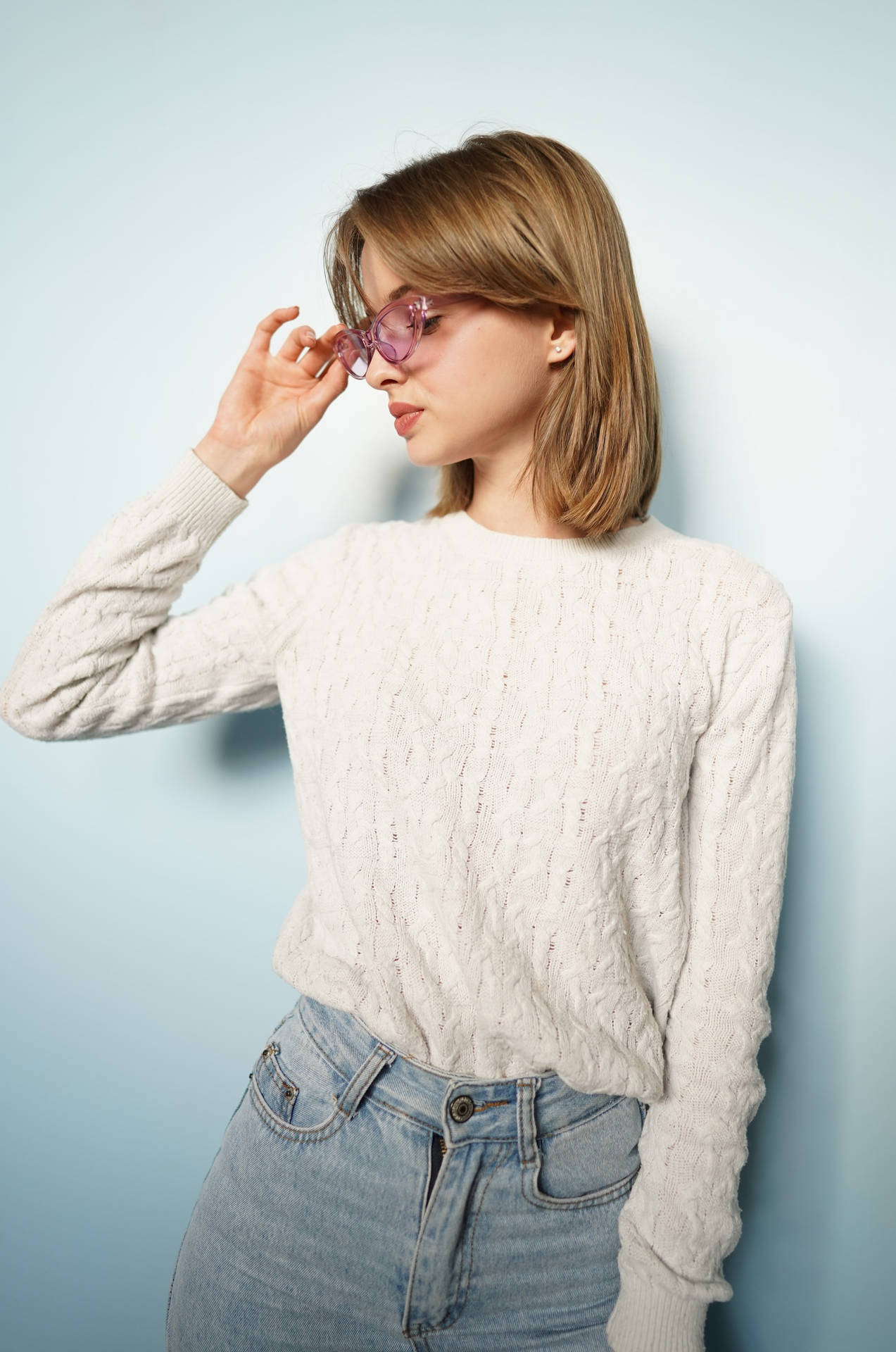 年輕女性在攝影棚調整粉紅色太陽眼鏡，穿著奶油色毛衣和牛仔褲